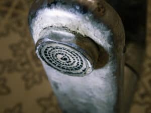 Hard water flows from an old tap aerator. Limescale, calcified shower water tap with lime scale in bathroom, Clogged Drains.