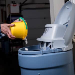 Yellow bucket pours salt pellets by a man into a water softener.