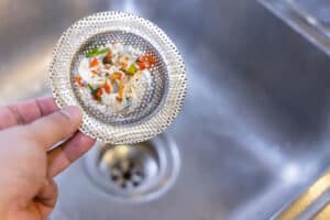 Hand holding kitchen sink waste filter with trapped food waste, Plumbing odors.