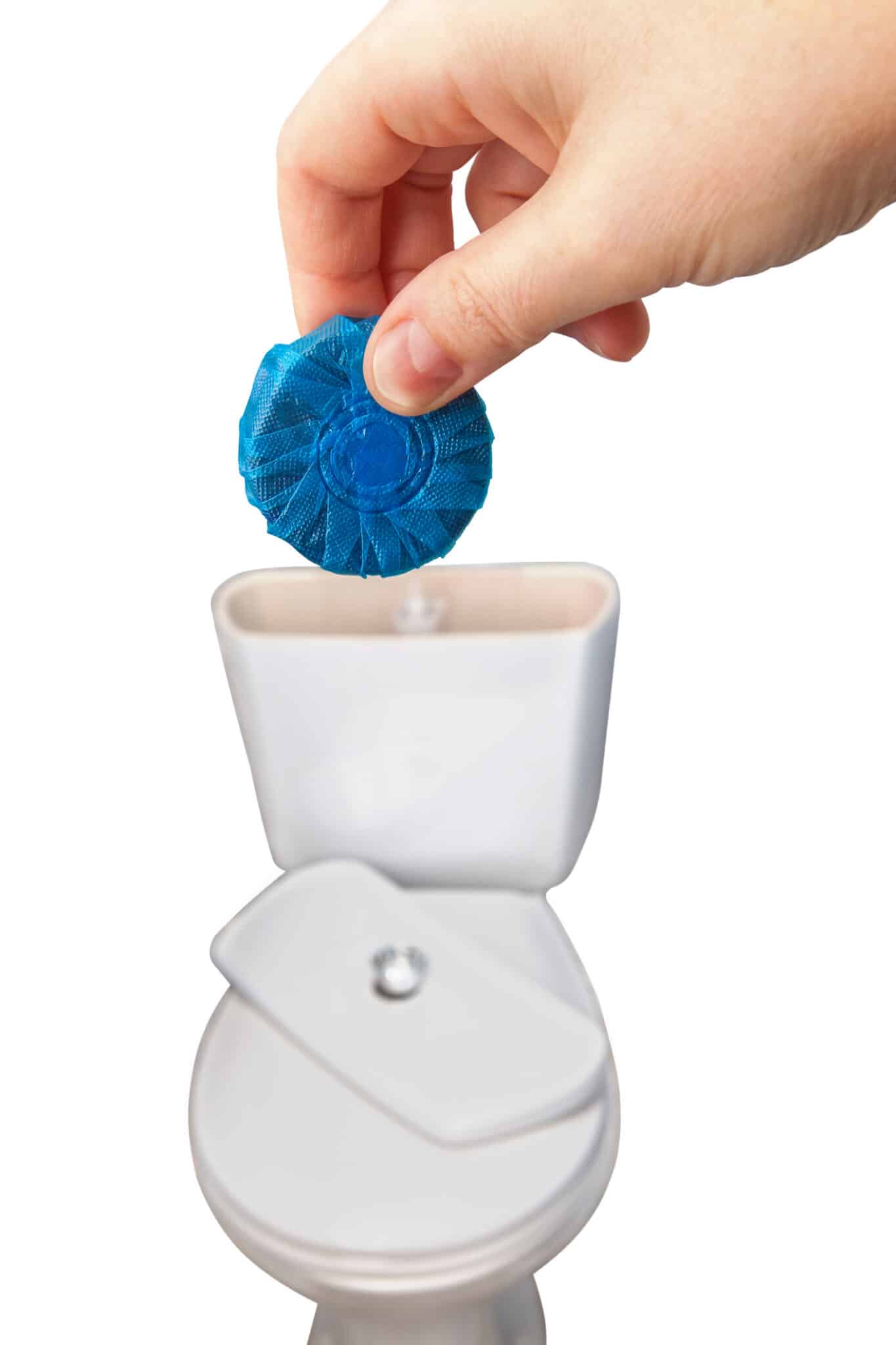 Close-up of hand pushes blue cleaning tablet into the toilet bowl drain tank, leak detection dye tablets.