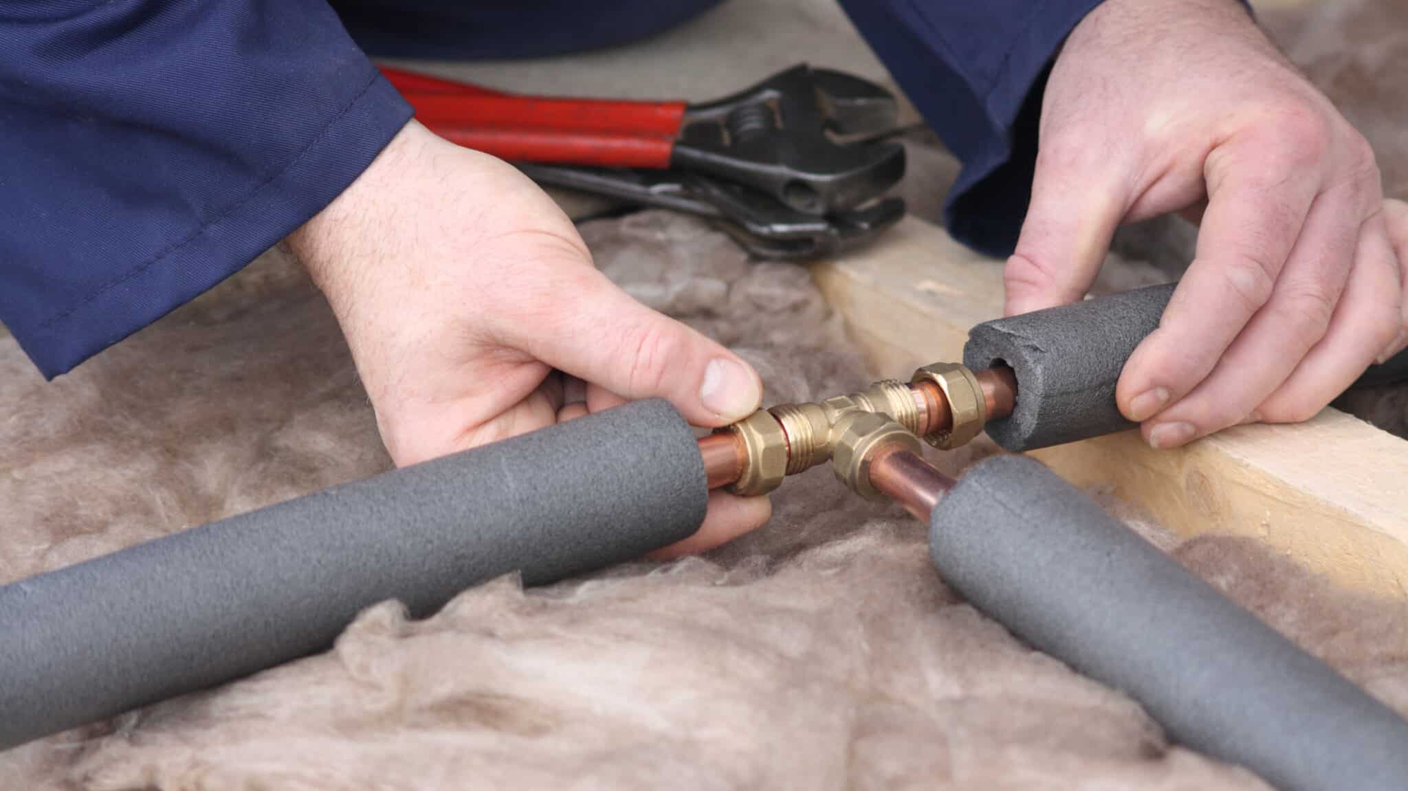 Plumber connecting three copper water pipes with insulation, smart winter plumbing protection.