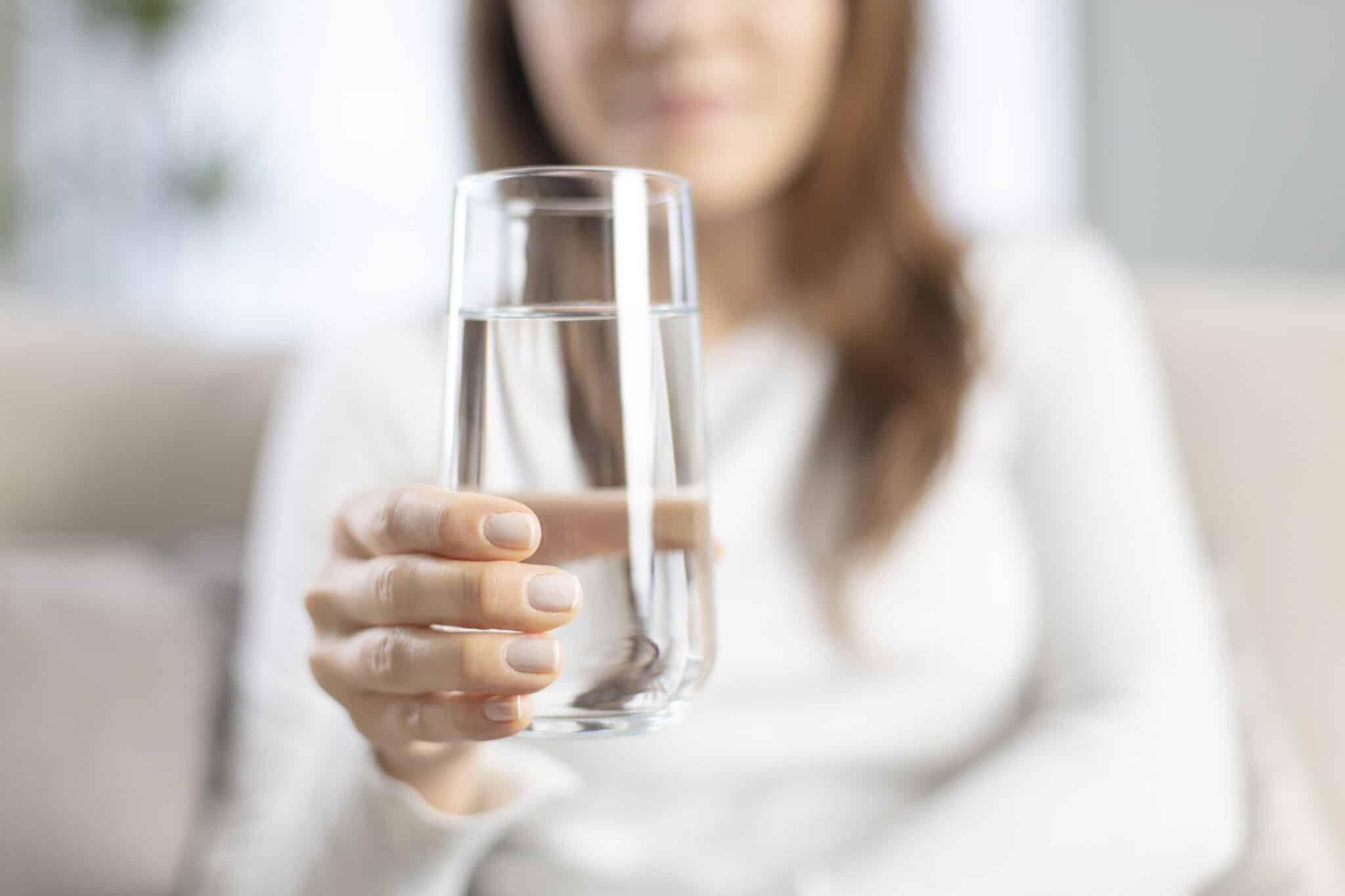 Woman drinking water at home, understanding water contaminants.