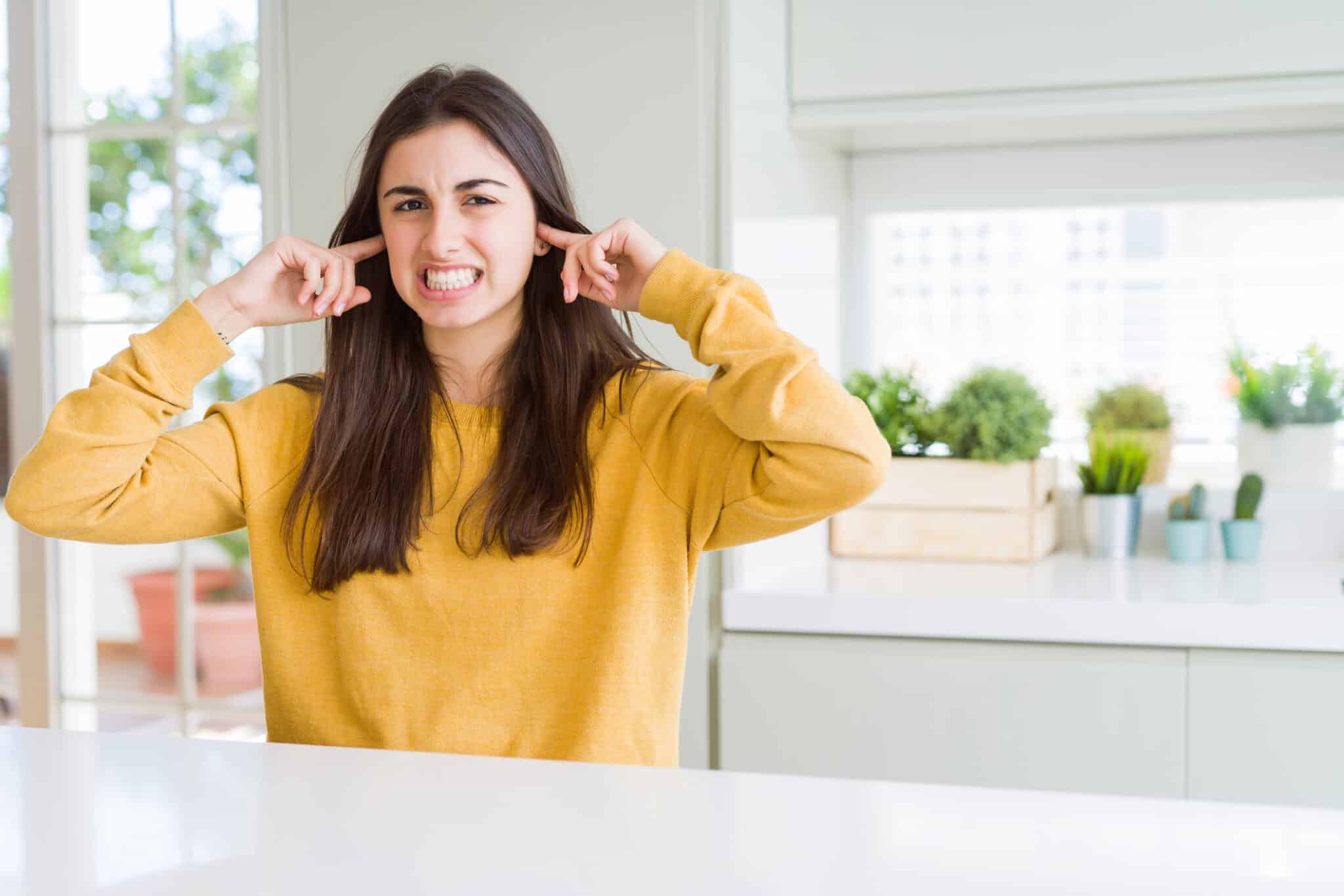 Woman wearing yellow sweater covering ears, noisy pipes, pipe vibration pads.
