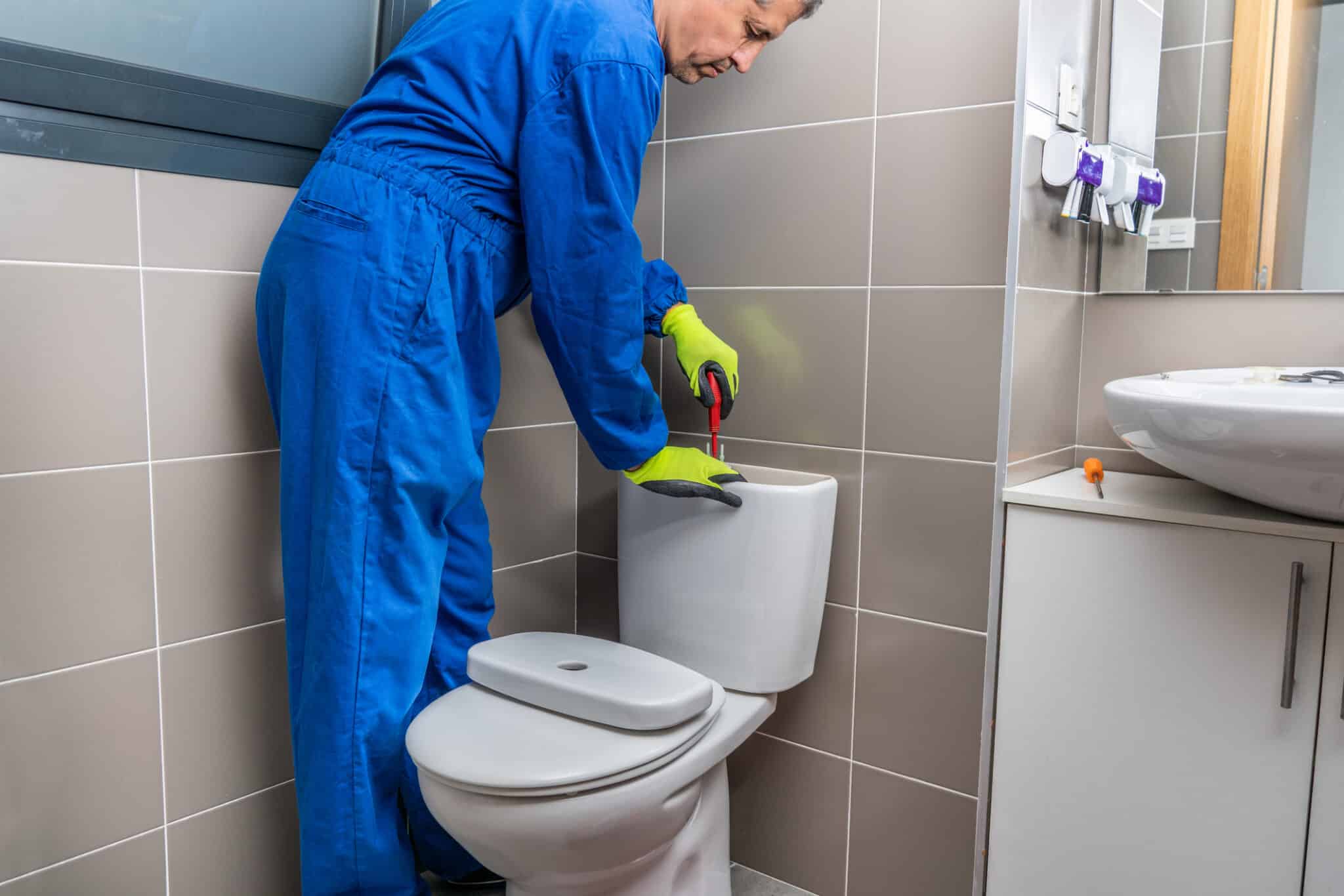 Clogged toilet help simple steps before calling a pro 2 Plumber fixing a toilet in the bathroom, clogged toilet help.